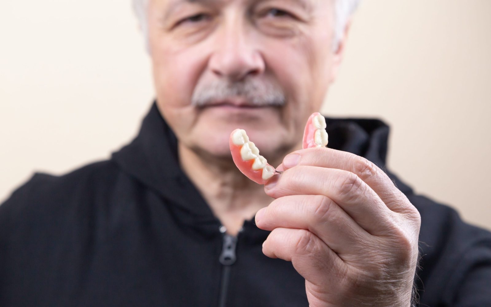 Image d'un homme âgé tenant son dentier partiel amovible avec un sourire satisfait sur son visage.