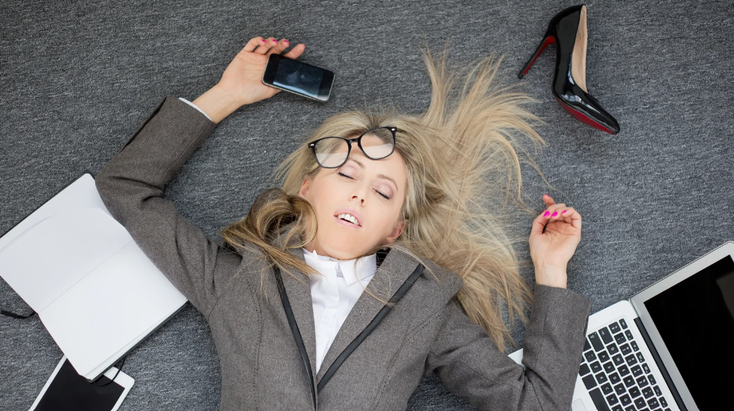 Femme en costume allongée sur le sol, épuisée, illustrant les effets du burnout et la nécessité de la gestion du stress pour les professionnels.